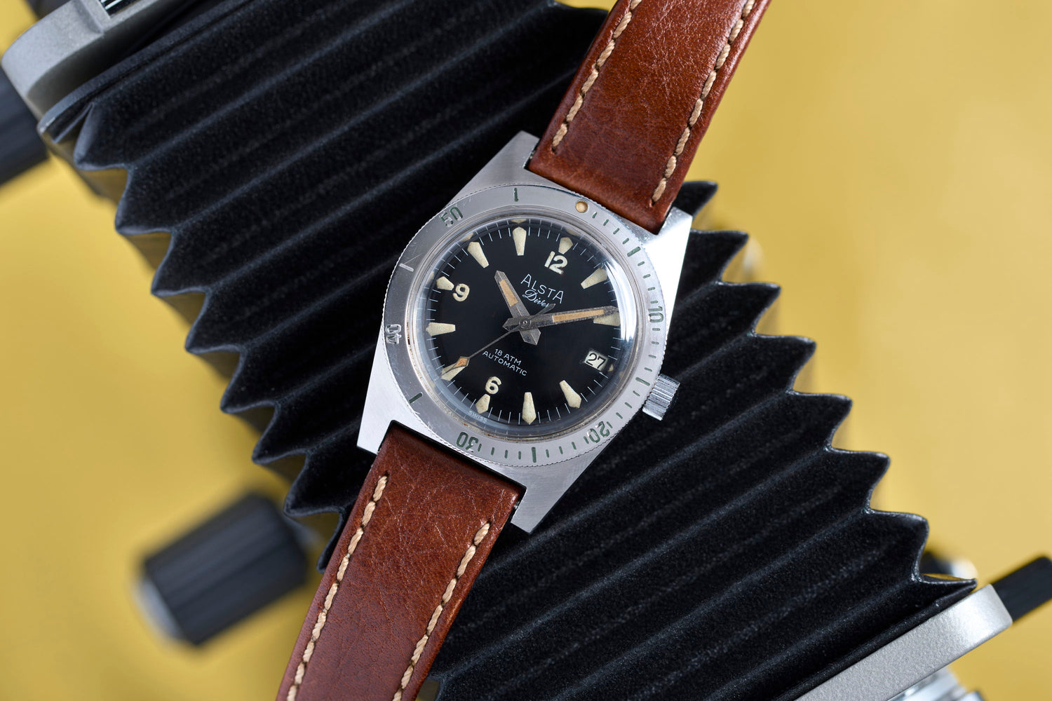 A vintage watch with a brown leather strap on a yellow background.