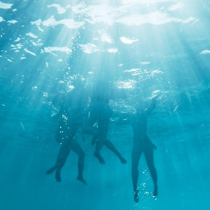 Three people swimming underwater with sunlight rays shining through the water.