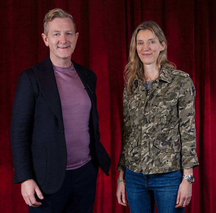 Two smiling individuals standing in front of a red curtain backdrop.